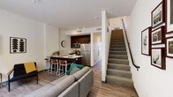 Located at 1006 South Main Street in Moscow, Idaho, this two-story unit at Identity Moscow offers a modern, functional layout designed with student living in mind. The main level opens into a combined living and kitchen area, where wood-look flooring flows throughout. The kitchen is outfitted with dark espresso cabinetry, stainless steel appliances including a full-size refrigerator, range, and microwave, and a breakfast bar with seating — ideal for both cooking and casual dining. The living area provides comfortable space for relaxing or gathering, with windows that bring in natural light. A carpeted staircase connects the two floors, leading to additional private bedrooms and bathrooms on the upper level. Bedrooms feature plush carpet, large windows with outdoor views of the surrounding Moscow streetscape and landscape, and dedicated desk areas for studying. Each bathroom is clean and compact, finished with wood-look flooring and a glass-enclosed walk-in shower. The overall design is contemporary and efficient, with a neutral color palette and thoughtful use of space throughout both floors, making this unit a well-rounded option for modern student living in Moscow, Idaho.