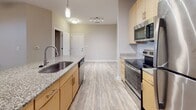 Located at 9101 Stony Point Pkwy in Richmond, Virginia, this single-floor residence offers a thoughtfully designed layout with modern finishes throughout. The open-concept kitchen serves as the heart of the home, featuring granite countertops, light wood cabinetry, stainless steel appliances including a refrigerator, range, microwave, and dishwasher, and a central island with a built-in sink. Pendant lighting and track lighting illuminate the space, while wood-look plank flooring flows seamlessly through the kitchen and living areas, adding warmth and cohesion. An elegant arched entryway connects the main living area to additional rooms, enhancing the architectural character of the space. The bedrooms are carpeted for comfort and include ceiling fans, natural light from window blinds, and generous closet storage. The bathrooms are finished with granite-topped vanities, light wood cabinetry, large mirrors, and tiled tub-shower combinations with curved curtain rods. A dedicated laundry area houses a full-sized washer and dryer with overhead shelving for added convenience. Neutral tones and clean lines throughout the space create a bright, modern ambiance suited for everyday living.