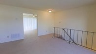 This inviting residential space is thoughtfully designed to offer comfort and functionality across its layout. The interior is finished with soft, wall-to-wall carpeting that adds warmth and a sense of coziness throughout. The upper landing area features a classic wrought iron stair railing, providing both safety and a subtle decorative touch as it guides the eye downward.

Adjacent to the landing, the living area is generously proportioned and bathed in natural light, courtesy of large windows dressed with vertical blinds that allow for flexible light control. A ceiling fan is centrally positioned in this area, ensuring year-round air circulation and comfort.

The walls throughout are finished in a clean, neutral tone, creating a versatile backdrop suitable for a variety of interior design styles. Flush-mounted light fixtures provide consistent overhead illumination, complementing the natural light that filters in from the windows.

Overall, the space presents a clean, well-maintained environment with practical features and a neutral aesthetic that makes it highly adaptable. The open sightlines between rooms enhance the sense of spaciousness, while the combination of natural and artificial lighting ensures the interior feels bright and welcoming throughout the day.