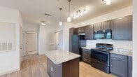 Located at 470 Bulldog Dr in Palm Coast, Florida, this one-bedroom, one-bathroom unit offers a thoughtfully designed single-floor layout that maximizes every square foot. The open-concept living area seamlessly combines the kitchen, dining, and living spaces into one cohesive area, creating an airy and functional environment. The kitchen is a standout feature, showcasing rich dark cabinetry, granite-style countertops, a central island with matching granite surface, pendant lighting, and black appliances including a gas range, refrigerator, and built-in microwave. Light wood-style flooring runs throughout the main areas, adding warmth and continuity to the space. The bedroom is generously sized, filled with natural light from dual windows with blinds, and equipped with a ceiling fan and two closets for ample storage. A hallway leads to the full bathroom, which features white tile flooring, a granite-topped vanity with dark cabinetry, and a tub-shower combination. Additional conveniences include a dedicated laundry area, multiple closets for storage, and a hallway connecting all areas efficiently. The clean white walls and bright lighting throughout lend the space a fresh, modern ambiance well-suited for comfortable everyday living.