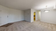 This single-floor residence offers a thoughtfully laid-out interior with distinct living, sleeping, and functional zones. The generously sized living room is finished with neutral wall-to-wall carpeting, white walls, and clean white baseboards, creating a bright and versatile space suited to a range of furniture arrangements. A pendant light fixture is visible near the dining area, adding a subtle decorative element to the open flow between rooms.

The kitchen is separated from the living area and features warm honey-toned wood cabinetry extending to the upper walls, providing ample storage. Dark granite-style countertops complement the cabinetry, while wood-look vinyl flooring adds warmth underfoot. White appliances, including a gas range, dishwasher, and refrigerator, are included, along with a stainless steel sink.

The bedroom is a comfortable, well-proportioned room with plush carpeting, a ceiling fan with light fixture, a window allowing natural light, and a closet. The neutral tones carry throughout, maintaining a cohesive aesthetic.

The bathroom is finished with beige square floor tiles and a full tub and shower combination enclosed by coordinating tile walls. A vanity with a medicine cabinet provides practical storage, keeping the space organized and functional.