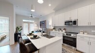 This well-designed one-bedroom, one-bathroom unit offers an efficient and thoughtfully organized single-level layout. The open-concept kitchen and living area form the heart of the space, creating a seamless flow ideal for both daily living and entertaining. The kitchen is appointed with crisp white shaker cabinetry extending to the ceiling, a gray tile backsplash, stainless steel appliances including a French-door refrigerator, electric range, and over-the-range microwave. A central island with an undermount sink and white quartz countertops provides additional prep space and casual seating. Wood-look flooring runs throughout the main living areas, adding warmth to the contemporary design. The living room benefits from abundant natural light through French doors fitted with blinds, and features a ceiling fan overhead. The bedroom is a comfortable retreat, carpeted for comfort, and connects directly to the bathroom. The bathroom is finished with white cabinetry, a quartz vanity top, framed mirror, and a decorative shower curtain, with additional built-in shelving for storage. A dedicated closet completes the unit's practical storage offerings. The overall aesthetic is clean, bright, and modern throughout.
