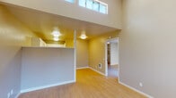 This single-floor residence offers a thoughtfully laid-out living space defined by clean lines, light-toned hardwood flooring, and a neutral color palette throughout. The main living area immediately impresses with its dramatic vaulted and double-height ceilings, drawing in natural light through elevated clerestory windows that enhance the sense of openness. A half-wall partition divides the living area from the kitchen zone, creating a subtle sense of definition while maintaining an open feel. The kitchen is efficiently designed with white cabinetry, white countertops, a stainless steel sink, and a full suite of white appliances including a range, dishwasher, and over-the-range microwave. Adjacent to the living area, a sliding glass door opens directly onto a private balcony, offering pleasant outdoor views and additional natural light. The bedroom is generously proportioned, featuring light hardwood flooring, a textured ceiling, and access to a walk-in closet with built-in shelving and a dresser. The bathroom is straightforwardly appointed with a shower-tub combination, toilet, and vanity. Throughout the space, consistent flooring and a warm, neutral tone create a cohesive and welcoming atmosphere suited to comfortable everyday living.
