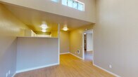 This single-floor residence offers a thoughtfully laid-out living space defined by clean lines, light-toned hardwood flooring, and a neutral color palette throughout. The main living area immediately impresses with its dramatic vaulted and double-height ceilings, drawing in natural light through elevated clerestory windows that enhance the sense of openness. A half-wall partition divides the living area from the kitchen zone, creating a subtle sense of definition while maintaining an open feel. The kitchen is efficiently designed with white cabinetry, white countertops, a stainless steel sink, and a full suite of white appliances including a range, dishwasher, and over-the-range microwave. Adjacent to the living area, a sliding glass door opens directly onto a private balcony, offering pleasant outdoor views and additional natural light. The bedroom is generously proportioned, featuring light hardwood flooring, a textured ceiling, and access to a walk-in closet with built-in shelving and a dresser. The bathroom is straightforwardly appointed with a shower-tub combination, toilet, and vanity. Throughout the space, consistent flooring and a warm, neutral tone create a cohesive and welcoming atmosphere suited to comfortable everyday living.