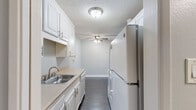 Located at 13495 Bancroft Ave in San Leandro, CA, this one-bedroom, one-bathroom residence offers a practical and well-appointed single-floor layout. Dark hardwood-style flooring runs throughout, providing a cohesive look that complements the neutral gray walls and crisp white trim found in every room.

The combined kitchen and living area forms the heart of the home. The galley-style kitchen is efficiently designed with white raised-panel cabinetry, light stone-look countertops, a stainless steel sink, and white appliances including a coil-top range, built-in microwave, dishwasher, and full-size refrigerator. A textured ceiling with a flush-mount light fixture keeps the space bright. The open living area offers generous room to arrange furnishings, enhanced by a ceiling fan, crown molding, and track lighting.

The bedroom is a comfortable, well-sized room featuring a wide horizontal window that fills the space with natural light and outdoor views of surrounding greenery. A dedicated walk-in closet with dual hanging rods provides ample storage.

The bathroom includes a white vanity with matching countertop, an undermount sink, and a separate water closet housing a full tub-shower combination with white tile surround. The textured ceilings and consistent flooring carry throughout, giving the entire residence a clean, uniform finish.