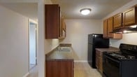 This single-floor residence offers a practical and comfortable layout designed for everyday living. The kitchen serves as a central feature of the home, showcasing warm wood cabinetry that provides ample storage both above and below the countertops. Dark granite-style counters run along the walls, offering generous prep space, and are complemented by a stainless steel sink. Black appliances, including a full-size refrigerator and range, add a cohesive, modern contrast to the rich wood tones throughout. The kitchen flooring features neutral tile that is both durable and easy to maintain. Flush ceiling lighting keeps the space bright and well-illuminated. A doorway visible from the kitchen hints at an open and connected floor plan, allowing for easy flow between the kitchen and the adjoining living areas. The neutral wall tones throughout create a clean, versatile backdrop that adapts well to a variety of furnishing styles. Overall, the space presents a straightforward, functional design that prioritizes practicality while maintaining a warm and inviting ambiance suitable for comfortable day-to-day living.
