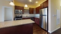 Located at 8 Digital Dr in Nashua, New Hampshire, this single-floor unit offers a thoughtfully designed layout with a seamless flow between living and functional spaces. The kitchen is a standout feature, showcasing rich dark wood cabinetry, granite-style countertops, a central island with pendant lighting, and a full suite of stainless steel appliances including a refrigerator, range, microwave, and dishwasher. Dark hardwood flooring grounds the kitchen with warmth and elegance. The open connection between the kitchen and living area creates an inviting, airy atmosphere, with the living space featuring neutral-toned carpet and access to natural light through large windows with exterior views. A hallway leads to multiple carpeted bedrooms, each offering a calm, neutral palette and natural light from windows overlooking the surrounding area. The walk-in closet is outfitted with wire shelving and rod storage, providing practical organization space with durable hardwood flooring. The bathroom features light tile flooring, dark wood vanity cabinetry, and granite-style countertops, maintaining a consistent design language throughout. Panel-style doors and clean white trim are consistent throughout, contributing to a cohesive and polished interior aesthetic.
