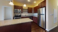 Located at 8 Digital Dr in Nashua, New Hampshire, this single-floor unit offers a thoughtfully designed layout with a seamless flow between living and functional spaces. The kitchen is a standout feature, showcasing rich dark wood cabinetry, granite-style countertops, a central island with pendant lighting, and a full suite of stainless steel appliances including a refrigerator, range, microwave, and dishwasher. Dark hardwood flooring grounds the kitchen with warmth and elegance. The open connection between the kitchen and living area creates an inviting, airy atmosphere, with the living space featuring neutral-toned carpet and access to natural light through large windows with exterior views. A hallway leads to multiple carpeted bedrooms, each offering a calm, neutral palette and natural light from windows overlooking the surrounding area. The walk-in closet is outfitted with wire shelving and rod storage, providing practical organization space with durable hardwood flooring. The bathroom features light tile flooring, dark wood vanity cabinetry, and granite-style countertops, maintaining a consistent design language throughout. Panel-style doors and clean white trim are consistent throughout, contributing to a cohesive and polished interior aesthetic.
