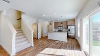 This two-story home offers a thoughtfully designed layout across two levels, with the majority of living space situated on the upper floor. The main level features an open-concept kitchen and living area anchored by a central island with granite countertops, pendant lighting, and stainless steel appliances including a range, microwave, and French-door refrigerator. Warm-toned hardwood-style flooring runs throughout the main level, complementing the neutral white walls and recessed lighting. A half bathroom on the main floor provides added convenience, and a dedicated laundry room houses a full-size washer and dryer. The attached garage features a concrete floor and direct interior access.

The upper floor accommodates all three bedrooms, including a generously sized primary bedroom with carpet flooring, a ceiling fan, two windows allowing natural light, and a walk-in closet with built-in shelving and hanging rods. Additional closets provide ample storage throughout. The four bathrooms are finished in a clean, neutral palette. Two hallways connect the upper-level rooms efficiently, and a carpeted staircase links the floors. The overall aesthetic is modern and understated, with consistent finishes creating a cohesive feel throughout.