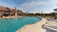 Located at 4285 Julep Way SW in Aiken, South Carolina, this outdoor amenity area is designed to deliver a resort-caliber experience for its residents. The centerpiece is a generously sized, curvilinear swimming pool filled with crystal-clear blue water, surrounded by a broad concrete pool deck that accommodates an extensive array of lounge chairs and shade umbrellas for sun-soaking and relaxation.

A covered cabana structure anchors one end of the pool area, featuring a distinctive metal roof and open-air design that provides a shaded retreat with seating for gatherings. The clubhouse building adjacent to the pool showcases attractive architectural details, including brick accents, a steep gabled roofline with a standing-seam metal roof, and large windows that blend a craftsman-inspired aesthetic with modern sensibility.

The surrounding landscape is carefully curated with ornamental grasses, palm trees, and tropical plantings that reinforce the resort atmosphere. A wrought-iron perimeter fence encloses the space, providing security while maintaining an open, airy feel. Views of the broader residential community are visible beyond the fencing, offering a sense of community integration. The entire outdoor space benefits from abundant South Carolina sunshine, creating a bright, inviting environment ideal for outdoor leisure year-round.
