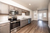 Located at 640 Marion Blvd in Marion, Iowa, this single-floor unit offers a clean, modern design throughout. The open-concept kitchen is a standout feature, equipped with a full suite of stainless steel appliances including a refrigerator, electric range, over-the-range microwave, and dishwasher. Rich, gray-toned cabinetry with brushed nickel hardware lines the walls, complemented by light countertops and recessed lighting above. Wood-look plank flooring runs seamlessly throughout the entire unit, adding warmth and continuity to every space. The living area is bright and open, benefiting from natural light streaming through multiple windows fitted with blinds. A glass-panel door provides direct access to a private outdoor balcony, enhancing the sense of openness. The bathroom is neatly appointed with a matching vanity cabinet and white countertop, a tub-shower combination, and consistent wood-look flooring that ties the space together. Neutral wall tones throughout the unit create a versatile backdrop suitable for a variety of interior styles. The layout is efficient and well-organized, with clear separation between the kitchen, living, and bathroom areas, making excellent use of the available footprint.