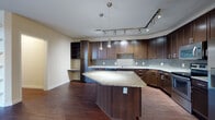 This single-floor residence is defined by a cohesive design aesthetic that balances contemporary finishes with functional living spaces. The kitchen serves as the centerpiece, showcasing rich dark-espresso cabinetry with sleek hardware, granite countertops, and a distinctive curved island that provides ample prep and gathering space. A mosaic tile backsplash adds texture, while stainless steel appliances—including a refrigerator, range, microwave, and dishwasher—deliver a polished, modern look. Track lighting and pendant fixtures illuminate the space effectively. A built-in desk or shelving nook adds a practical workspace element.

The living area features dark hardwood-style flooring and benefits from natural light through large windows and glass doors that open to an outdoor area. Built-in open shelving provides an attractive display and storage feature along one wall.

Bedrooms are finished with neutral carpet, ceiling fans, and windows that invite natural light and outdoor views. The bathrooms maintain the design consistency with dark cabinetry vanities, white countertops, tile-surround tub-shower combinations, and coordinating hardwood-style flooring, creating a clean and modern aesthetic throughout.