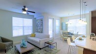 Located at 320 The Green Cir in Raleigh, NC, this single-floor residence offers a welcoming and well-lit interior defined by an open-concept layout that seamlessly connects the living and dining areas. Large windows dressed with white horizontal blinds flood the space with abundant natural light, creating an airy and inviting atmosphere throughout.

The living area is comfortably proportioned, featuring light-toned carpet flooring and a ceiling fan that adds both functionality and a casual aesthetic. A patterned area rug anchors the seating arrangement, which centers around a classic sofa accented with decorative pillows. The neutral wall tones enhance the brightness of the room and provide a versatile backdrop for varied décor styles.

Adjacent to the living space, the dining area transitions smoothly, highlighted by an elegant pendant chandelier that adds a touch of sophistication. The dining setup accommodates a generous number of seats, making it suitable for both everyday meals and entertaining. A door with glass panels allows additional natural light to enter while providing access to the outdoors. Together, the rooms convey a cohesive, comfortable, and functional living environment.