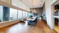 Located at 660 Quayside Dr in New Westminster, BC, this elegantly designed amenity space delivers a refined and upscale atmosphere across a single, open-concept floor. Warm hardwood flooring runs throughout, complementing the modern aesthetic and tying together the distinct functional zones seamlessly.

The kitchen is a standout feature, showcasing sleek slate-toned cabinetry paired with dark countertops and a dramatic floor-to-ceiling swirling stone feature wall that serves as a bold artistic focal point. A stainless steel range and hood add a professional-grade touch, while a dark island with bar seating provides additional workspace and casual gathering space.

The dining area is anchored by a long, polished white stone communal table surrounded by contemporary black chairs, ideal for group gatherings. Two sculptural brass-and-glass globe chandeliers hang overhead, adding warmth and visual drama to the space.

Adjacent to the dining area, a comfortable lounge zone is bathed in abundant natural light streaming through expansive floor-to-ceiling windows, offering panoramic views of the surrounding New Westminster skyline and waterfront. A textured mosaic feature wall adds depth and contrast to the bright, airy atmosphere.

Together, these elements create a cohesive, design-forward space that balances sophistication with functionality.