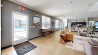 This well-appointed community clubhouse, developed by LDG Development, is located at 10605 Newtown Woods Trail in Louisville, KY. The single-floor facility offers a generous and thoughtfully designed layout spread across multiple functional areas. Guests are welcomed through a glass-door entry foyer displaying the LDG Development signage, with light tile flooring and a clean, professional aesthetic setting the tone throughout.

The interior features two comfortable living rooms with light hardwood-style flooring, crown molding, and neutral tones that create a warm and inviting atmosphere. Tasteful artwork and soft seating arrangements make these areas ideal for relaxing or socializing. A well-lit reception area with vaulted ceilings and large windows provides ample natural light and outdoor views.

The combined kitchen and living room area is equipped with dark cabinetry, granite countertops, stainless steel appliances, and a spacious island — making it suitable for community gatherings and events. An adjacent dining room offers a dedicated space for shared meals. Two connecting hallways ensure smooth circulation throughout the facility, while a private conference room with a round table and natural window light serves as a versatile meeting space. Rounding out the amenities is a dedicated exercise room outfitted with free weights, a bench, and fitness equipment.