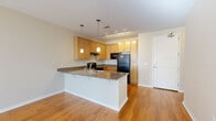 Located at 2775 S Brook Dr in Denver, CO, this single-floor residence offers a well-designed, open-concept layout that seamlessly connects the living and kitchen areas. The kitchen is a standout feature, equipped with light maple cabinetry, granite-style countertops, black appliances including a refrigerator, electric range, and dishwasher, and an extended peninsula with pendant lighting overhead. Warm hardwood flooring runs throughout the main living areas, complementing the neutral color palette and creating a bright, welcoming ambiance. The living area benefits from natural light streaming through large windows and a glass door that leads to an outdoor access point. The bedrooms are carpeted for comfort and each includes a closet with built-in hanging rods, offering practical storage solutions. The bathroom is thoughtfully appointed with a single-sink vanity featuring wood cabinetry and dark countertop, a large wall mirror, tile flooring, and a glass-enclosed walk-in shower. A dedicated in-unit laundry room accommodates a full-size washer and dryer side by side, with additional built-in shelving for storage. The overall design is clean and functional, making this a practical and comfortable space in a convenient Denver location.