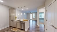 Located at 6805 Walnut Branch Lane in Charlotte, NC, this well-appointed one-bedroom, one-bathroom unit offers a thoughtfully designed layout across a single floor. The open-concept kitchen serves as a centerpiece, featuring light wood cabinetry, sleek quartz countertops, stainless steel appliances, and a peninsula island with pendant lighting overhead — ideal for both cooking and casual dining. Wood-style flooring flows throughout the main living areas, adding warmth and continuity to the space. The living area is illuminated by natural light from large windows and a glass balcony door, with a ceiling fan providing comfort year-round. The private balcony overlooks a landscaped courtyard framed by a multi-story residential building, offering a pleasant outdoor retreat. The bedroom is carpeted for comfort, features a ceiling fan and a window with exterior views, and connects conveniently to a dedicated closet. The bathroom is finished with large-format tile, a glass-enclosed walk-in shower, and coordinating wood-toned cabinetry. An in-unit laundry area and a hallway complete the functional layout, making this a compact yet efficiently organized living space.