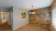 This single-story, two-bedroom, two-bathroom unit offers a well-organized layout across a comfortable footprint. The living area serves as the heart of the space, featuring large windows flanking the front entry door that allow generous natural light to fill the room. Carpet flooring extends throughout the living and bedroom areas, lending warmth underfoot.

The dining area is a standout space, distinguished by a full exposed brick accent wall that adds striking texture and character. An elegant chandelier hangs overhead, complementing the rustic appeal of the brickwork. A pass-through window connects the dining area directly to the kitchen, enhancing the flow between spaces.

The kitchen is equipped with warm wood cabinetry, dark granite-style countertops, a stainless steel sink, and a gas range, offering practical functionality with hardwood-style flooring.

Both bedrooms are carpeted and feature neutral gray walls, ceiling-mounted light fixtures, and ample space. The primary bedroom includes a ceiling fan and a window providing natural light. Each bathroom is outfitted with a single-sink vanity with light countertops, tile flooring, and white cabinetry, with one bathroom featuring a full tub-shower combination.