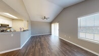 This single-story home offers a well-designed layout with a blend of modern finishes and functional living spaces throughout. The open living area immediately impresses with soaring vaulted ceilings and a ceiling fan overhead, creating an airy, spacious atmosphere. Dark wood-style flooring extends throughout the main living areas, complemented by neutral gray walls and crisp white baseboards. Large sliding glass doors flood the living space with natural light and provide access to the outdoors, while additional windows along the front of the home enhance brightness.

The kitchen is thoughtfully designed with a galley-style layout featuring granite countertops, gray lower cabinetry, white upper cabinets, a stainless steel sink, and a full suite of stainless steel appliances. A dedicated in-unit laundry area accommodates a full-size washer and dryer side by side.

The bedrooms are carpeted for comfort and offer generous proportions, with one room featuring a closet with built-in shelving. The bathroom is well-appointed with gray cabinetry, granite countertops, a large vanity mirror, and a shower-tub combination. Throughout the home, the consistent use of neutral tones and quality finishes creates a cohesive and move-in ready environment.