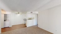 Unit #403 at 444 4th in Escondido offers a practical and well-organized single-floor layout with a clean, neutral aesthetic throughout. The open living and dining area is finished with plush wall-to-wall carpeting and features a ceiling fan with light fixture, a textured ceiling, and a sliding glass door that fills the space with natural light and provides outdoor access. The galley-style kitchen is efficiently designed with white cabinetry lining both sides, offering ample storage, granite-toned laminate countertops, a double-basin stainless steel sink, and white appliances including a range and refrigerator. A pass-through peninsula connects the kitchen to the main living area, enhancing the open feel of the shared space. The bedrooms are carpeted and bathed in natural light from windows with outdoor views of surrounding greenery. The bathroom is cleanly finished with a tiled tub-and-shower combination, granite-toned countertops, a vanity with mirror, and wood-look flooring. A separate water closet provides added privacy. In-unit laundry hookups are also visible, adding everyday convenience. The overall palette of white walls, light carpeting, and bright finishes gives the unit a fresh, move-in-ready appearance.