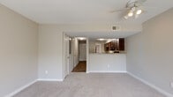 This two-story unit at Watermark Place in Columbia, SC offers a practical and well-organized layout spread across two floors. The main floor houses the combined kitchen and living area, a hallway, and a half bathroom. The open-concept design connects the carpeted living room to the kitchen, which is separated by a breakfast bar with granite-style countertops. The kitchen features rich dark-brown cabinetry, matching granite countertops, black appliances including a refrigerator, dishwasher, and range, and wood-look tile flooring. A ceiling fan with lighting fixtures is installed in the living area. The entry hallway features wood-look flooring and louvered closet doors, leading to a carpeted staircase that connects to the upper floor. Upstairs, two bedrooms are finished with plush carpeting and neutral-toned walls. The spacious primary bedroom includes two windows offering outdoor views, while the secondary bedroom features a single window with natural light. The upper floor also contains two full bathrooms, each finished with dark vanity cabinetry, granite-style countertops, wood-look tile flooring, and a tub-shower combination. The overall aesthetic is clean and neutral throughout.