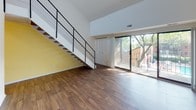 This two-story residence in Detroit, Michigan offers a well-organized layout spanning one bedroom, a loft, and one and a half bathrooms. The main level features wood-look flooring throughout the living and kitchen areas, creating a warm, cohesive aesthetic. A striking open-riser staircase with black metal railings connects the floors and serves as a visual focal point. Soaring ceilings amplify the sense of openness, while a sliding glass door floods the living area with natural light and provides direct access to a private balcony overlooking a community pool.

The kitchen is equipped with oak cabinetry, a dishwasher, a double sink, and a bold accent wall, complemented by a built-in pantry column for added storage. A half bathroom on the main level features tile flooring, a wood vanity, and a stone-topped countertop with a mirrored medicine cabinet.

Upstairs, the carpeted bedroom features vaulted ceilings, a window for natural light, and access to a walk-in closet with built-in shelving. The full bathroom includes a tiled tub-shower combination, a wood vanity, and stone-look tile flooring. The adjacent loft space, also carpeted with a sloped ceiling, offers flexible use as an office or additional living area.