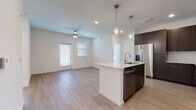This single-floor unit showcases a contemporary design with a cohesive blend of modern finishes and functional layout. The open-concept living and kitchen area serves as the heart of the space, featuring light-toned hardwood-style flooring that extends throughout the main areas. A ceiling fan overhead and multiple windows with slatted blinds allow natural light to fill the living space, creating a bright and airy atmosphere.

The kitchen is a standout feature, centered around a substantial island with a granite countertop and an integrated sink with a brushed nickel faucet. Dark espresso cabinetry lines the walls, contrasting elegantly with a classic white subway tile backsplash. Stainless steel appliances, including a refrigerator with an ice and water dispenser, electric range, microwave, and dishwasher, complete the well-appointed kitchen.

The bedrooms offer plush carpeting and ceiling fans, with generously sized windows that invite natural light. The primary bathroom is finished with a dark wood vanity topped with granite, a large framed mirror, hardwood-style flooring, and a soaking tub surrounded by crisp white subway tile. A walk-in closet provides ample storage. The overall design is clean, modern, and move-in ready.