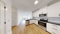 This thoughtfully designed single-floor residence at 43 Lakeside Ave in Pompton Lakes, NJ offers a bright, modern aesthetic with a cohesive palette of white walls, warm light wood flooring, and sleek black hardware throughout. The open-concept kitchen flows seamlessly into the living area and features white shaker-style cabinetry, dark countertops, a classic subway tile backsplash, and a full suite of stainless steel appliances, including a range, over-the-range microwave, dishwasher, and refrigerator. Recessed lighting illuminates the space, while a large multi-pane window in the living area allows generous natural light to fill the room. The bedrooms are well-proportioned and include ample closet storage, with one bedroom offering a walk-in closet with built-in shelving and hanging rods. A second bedroom provides a double-door closet. The primary bedroom connects to an en-suite bathroom with a glass-enclosed shower and tiled walls, while a second bathroom features a tub/shower combination with floor-to-ceiling tile surround, a white vanity, and dark countertop. The overall ambiance is clean, contemporary, and move-in ready.