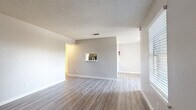 This well-appointed single-story, one-bedroom, one-bathroom unit offers a practical and comfortable layout across a thoughtfully organized floor plan. The combined kitchen and living area forms the heart of the home, featuring light-toned luxury vinyl plank flooring, neutral gray walls, and a textured ceiling throughout. A charming pass-through window connects the kitchen to the living room, enhancing the open feel of the space. The galley-style kitchen is equipped with white cabinetry featuring brushed nickel hardware, light countertops, a stainless steel sink, a dishwasher, and black appliances including an electric range and refrigerator, all illuminated by overhead lighting. Natural light filters into the living area through window blinds, adding brightness to the neutral palette. The bedroom is generously sized, finished with plush carpet, a ceiling fan with light kit, and a window for natural light. A walk-in closet with built-in shelving and hanging rods provides ample storage. The full bathroom features a tub-shower combo with white tile surround, wood-look vinyl flooring, a toilet, and a vanity with a marble-style countertop. Clean finishes and a cohesive neutral color scheme give the entire unit a fresh, move-in-ready appearance.