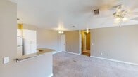 This single-story unit in Ridgeland, Mississippi offers a practical, open-concept layout that connects the main living area directly to the kitchen. The living space features neutral-toned carpet and textured ceilings, with a chandelier providing overhead lighting. A ceiling fan with light fixture is present in one of the bedrooms, which also benefits from a window that allows natural light to filter in.

The kitchen is equipped with white cabinetry offering ample storage, granite-look countertops, a double-basin stainless steel sink, a dishwasher, an electric range, and a full-size refrigerator. A peninsula counter separates the kitchen from the living area, adding functional workspace and a natural division between the two zones. The kitchen and adjoining utility areas feature wood-look hard surface flooring, contrasting with the carpet found throughout the living and sleeping spaces.

The bathroom includes a combination tub and shower, a single-sink vanity with white cabinetry, and wood-look flooring. A dedicated laundry room provides upper cabinet storage, a window for natural light, and utility hookups. The bedrooms are carpeted, neutral in tone, and offer comfortable proportions suitable for standard furnishings.