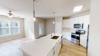 This single-story home presents a clean, modern aesthetic defined by a neutral color palette, light wood-look flooring, and an open, flowing layout. The kitchen serves as the centerpiece of the living space, anchored by a generously sized island with a white quartz countertop and an undermount sink, illuminated by elegant pendant lights. White shaker-style cabinetry lines the walls, offering ample storage, while stainless steel appliances—including a refrigerator, electric range, built-in microwave, and dishwasher—add a polished, contemporary finish. A subway tile backsplash and skylight further brighten the cooking area. The kitchen opens directly to the living area, creating a seamless, social atmosphere suited to everyday living and entertaining. Bedrooms feature the same warm wood-look flooring, ceiling fans, and windows fitted with blinds that frame outdoor greenery views, allowing natural light to fill the space. The primary bathroom includes a dual-sink vanity topped with white counters, shaker-style cabinetry, brushed nickel fixtures, and a large wall mirror flanked by modern sconce lighting. Throughout the home, crisp white trim, neutral walls, and consistent finishes create a cohesive, well-maintained environment.