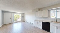 Located at 1920 NE Merman Dr in Pullman, Washington, this one-bedroom, one-bathroom unit offers a thoughtfully arranged single-floor layout. The combined kitchen and living area forms the heart of the unit, finished with light wood-style flooring that creates a clean, cohesive look throughout. Large windows allow generous natural light to fill the space, with a wall-mounted air conditioning unit and baseboard heating providing year-round climate control.

The kitchen is outfitted with white shaker-style cabinetry, both upper and lower, complemented by light countertops and a full suite of black appliances including a refrigerator, electric range, over-the-range microwave, and dishwasher. A sink with a window view adds practicality to the workspace.

A hallway connects the main living area to the bedroom and bathroom. The bedroom features plush carpeting, a ceiling fan with integrated light fixture, a window with vertical blinds, and baseboard heating. The bathroom includes wood-style flooring, a vanity with sink, and a tiled shower/tub area. Neutral wall tones and textured ceilings are consistent throughout, lending the unit a simple, functional aesthetic well-suited to Pullman living.