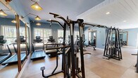 Located on Legends Drive in Southern Pines, NC, this well-appointed exercise facility offers a generously sized, single-floor layout designed to accommodate a full range of fitness activities. The space is divided into distinct functional zones, seamlessly connected to create an open yet organized environment.

The strength and cardio area features durable, neutral-toned flooring and is equipped with a comprehensive selection of machines, including treadmills, ellipticals, cable systems, a power rack, and weight benches. Soft blue walls, recessed lighting, and large windows allow natural light to filter in, creating an energizing atmosphere with views of the surrounding greenery.

A dedicated studio zone transitions to warm hardwood-style flooring and is accented by exposed white wood-beam ceilings with shiplap detailing, lending a refined, architectural character to the space. Full-length mirrors in rich wood frames line the walls, amplifying the sense of openness, while wall-mounted sconce lighting adds warmth. This area is well-suited for stretching, yoga, or group fitness activities.

Throughout the facility, white shiplap ceiling treatments and soft blue-gray walls maintain a cohesive, upscale aesthetic. French doors and interior windows connect zones fluidly, while organized storage solutions and a medicine ball rack ensure the space remains functional and tidy. The overall design balances practicality with polished, inviting finishes.
