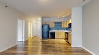 Located at 128 W Mishawaka Ave in Mishawaka, Indiana, this single-floor unit presents a clean, contemporary design carried consistently throughout its layout. Wood-look plank flooring flows seamlessly across the living and sleeping areas, providing a warm, cohesive foundation. The open-concept living area is spacious and airy, painted in soft neutral tones with a ceiling fan overhead, allowing comfortable airflow. The kitchen sits adjacent to the living space and features light maple cabinetry with brushed silver hardware set against a distinctive teal accent wall. Black appliances — including a refrigerator, dishwasher, electric range, and over-the-range microwave — complement the contemporary palette, while white countertops and a stainless steel sink provide functional workspace. Track lighting illuminates the kitchen effectively. The bedrooms are bright and well-proportioned, each featuring wood-look flooring, neutral walls, and windows with blinds that invite natural light. One bedroom benefits from a corner window arrangement, enhancing the sense of openness. The bathrooms are finished with light wood vanities, white countertops, large mirrors, and a tub-shower combination with chrome fixtures, maintaining the unit's consistent, modern aesthetic throughout.