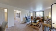 This single-floor residence offers a thoughtfully arranged layout with distinct living, dining, sleeping, and kitchen areas. The living room is a comfortable, carpeted space featuring a large window with green drape panels that invite natural light and outdoor views. A glass-top TV console, cushioned sofa, patterned area rug, and framed wall art contribute to the room's welcoming atmosphere. A hallway connects the living area to the rest of the home.

The dining room features tile flooring, a ceiling fan with light fixture, and a window dressed with layered curtains. A dark wood dining table with matching chairs serves as the focal point, complemented by a buffet sideboard along the wall.

The kitchen is efficiently designed with warm wood cabinetry, granite-style countertops, and black appliances including a gas range, dishwasher, and refrigerator, all set on tile flooring.

The primary bedroom offers carpeted floors, dual windows, and ample space for a full dresser setup. A secondary bedroom, also carpeted, includes a window with natural light. The bathroom features white wall tile, a vanity with wood cabinetry, tile flooring, and a tub-shower combination.