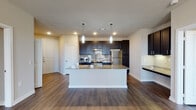 Located at 401 Coit Rd in McKinney, Texas, this single-story residence offers a well-designed open-concept layout that seamlessly connects the kitchen, dining, and living areas. The kitchen is a standout feature, showcasing rich dark cabinetry, granite countertops, a large central island with an undermount sink, pendant lighting, a subway tile backsplash, and a full suite of stainless steel appliances including a refrigerator, range, and microwave. Recessed lighting and under-cabinet lighting enhance the kitchen's functionality and ambiance. Wood-look plank flooring extends throughout the unit, adding warmth and cohesion to every room. The living area benefits from a ceiling fan and a window that invites natural light and outdoor views. Bedrooms are generously sized with large windows overlooking the surrounding landscape. The bathrooms are thoughtfully finished, with one featuring a granite-topped dark vanity with ample storage and a linen tower, and another offering a full soaking tub with floor-to-ceiling tile surround and wood-look flooring. Neutral wall tones and clean white trim throughout create a bright, modern atmosphere well-suited for comfortable everyday living.
