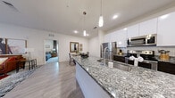 Located at 5110 S Manhattan Ave in Tampa, FL, this single-floor residence offers a thoughtfully designed open-concept layout with modern finishes throughout. The kitchen serves as a central focal point, showcasing expansive granite countertops, a large island with a stainless steel undermount sink, white upper cabinetry paired with dark lower cabinets, a subway tile backsplash, and a full suite of stainless steel appliances. Pendant lighting above the island adds a refined touch. The adjoining dining area is an intimate space with warm neutral tones, wood-look flooring, and decorative wall art. The living room is bright and welcoming, featuring large windows and French doors that invite abundant natural light, complemented by light hardwood-style flooring and floor-to-ceiling draping. The primary bedroom offers plush carpeting, generous closet space, and softly filtered natural light. A second bedroom provides a comfortable, well-appointed space equally suited for guests or a home office. Both bathrooms are finished with granite vanity countertops, dark wood cabinetry, large format tile flooring, full tub-shower combinations, and oversized mirrors. The overall ambiance is clean, contemporary, and cohesive, with a neutral palette that creates a bright and inviting atmosphere throughout.