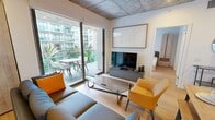 This contemporary 830 square foot apartment, located in the TENTEN Downtown complex, offers a harmonious blend of modern amenities and industrial-chic design. The space comprises two bedrooms, two bathrooms, and an open-concept living area, all thoughtfully arranged on a single floor.

The kitchen is a standout feature, boasting a sleek design with two-tone cabinetry - light wood upper cabinets contrasting with dark lower units. Stainless steel appliances, including a side-by-side refrigerator and built-in microwave, complement the space. A textured white backsplash adds visual interest, while under-cabinet lighting enhances functionality.

The primary bedroom, measuring 170 square feet, showcases exposed concrete walls and ceilings, creating an urban loft aesthetic. Large windows allow for ample natural light and offer views of the surrounding cityscape. The second bedroom maintains a similar style, with white walls providing a neutral backdrop.

Both bathrooms feature a modern design with clean lines. Glass-enclosed showers, floating vanities, and large mirrors contribute to a sense of spaciousness. The apartment's industrial theme is carried through with exposed ductwork and concrete ceilings throughout.

A key highlight is the private balcony, accessible from the living area, offering outdoor space and views of the complex's central courtyard. The TENTEN Downtown's exterior showcases a striking architectural design with multiple levels of balconies, creating a dynamic facade.

This apartment seamlessly combines functionality and style, perfect for those seeking a contemporary urban living experience.