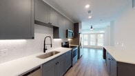 Located at 218 W Commerce St in Dallas's vibrant Bishop Arts District, this single-story unit showcases a contemporary design with a cohesive, open-concept layout and warm wood-look flooring throughout. The kitchen serves as a focal point, outfitted with slate-gray shaker cabinetry extending to the ceiling, crisp white quartz countertops, and a herringbone-patterned tile backsplash. A matte black spring-neck faucet accents the undermount stainless steel sink, while stainless steel appliances — including a range, over-the-range microwave, refrigerator, and dishwasher — complete the functional space. Under-cabinet lighting adds a polished finishing touch. The kitchen flows seamlessly into the open living area, where a ceiling fan circulates air and elegant French doors flood the space with natural light while providing outdoor access. The bathroom features white subway tile surrounding the tub and shower area, complemented by matte black fixtures for a refined, modern aesthetic. Adjacent to the bathroom, a walk-in closet offers generous built-in shelving and double hanging rods, providing practical and well-organized storage. Recessed lighting throughout the unit ensures consistent illumination, while the clean white walls and open layout create a bright, welcoming ambiance well-suited to the energy of the surrounding neighborhood.
