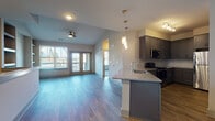 This thoughtfully designed two-story residence offers a seamless blend of modern finishes and functional layout across two well-defined levels. The main living area is open-concept, anchored by durable hardwood-style flooring that flows throughout the space. A ceiling fan and large French doors bathe the living room in natural light while providing access to the outdoors. The kitchen is a standout feature, outfitted with dark gray shaker-style cabinetry, granite countertops, stainless steel appliances including a refrigerator and microwave, a black range, and a kitchen island with pendant lighting overhead — ideal for both cooking and casual dining. A dedicated dining or flex area nearby benefits from built-in open shelving, adding both storage and architectural character. Upstairs, a carpeted bedroom provides a quiet retreat with a generously sized window that frames neighborhood views. The bathroom is finished with large-format tile surrounding the soaking tub and shower, a granite-top vanity, and wood-look flooring. The lower level includes a spacious attached garage with an automatic opener, offering secure and convenient parking. Throughout, the space maintains a clean, contemporary aesthetic with neutral tones and quality finishes.