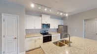 Located at 557 Roanoke Rd in Daleville, Virginia, this single-floor unit offers a well-designed, open layout with thoughtful finishes throughout. The kitchen serves as a central highlight, showcasing white shaker-style cabinetry, light granite countertops, and a full suite of stainless steel appliances including an electric range, over-the-range microwave, and refrigerator. A kitchen island with a deep double-basin sink provides additional workspace and serves as a natural transition into the open living area. Track lighting overhead ensures the kitchen is well-illuminated throughout.

The living area features wood-look plank flooring, neutral wall tones, and a ceiling fan with light fixture. A glass-paned exterior door invites natural light and connects the interior to the outdoors. The open sightlines between the kitchen and living space create an airy, connected feel.

The bedroom is finished with plush wall-to-wall carpeting, a ceiling fan, and a window that brings in additional natural light. A generously sized walk-in closet with wire shelving systems provides ample storage. The bathroom includes a full tub-shower combination with a curved rod, wood-look vinyl flooring, and a white vanity, maintaining the clean, consistent aesthetic found throughout the unit.