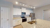 Located at 557 Roanoke Rd in Daleville, Virginia, this single-floor unit offers a well-designed, open layout with thoughtful finishes throughout. The kitchen serves as a central highlight, showcasing white shaker-style cabinetry, light granite countertops, and a full suite of stainless steel appliances including an electric range, over-the-range microwave, and refrigerator. A kitchen island with a deep double-basin sink provides additional workspace and serves as a natural transition into the open living area. Track lighting overhead ensures the kitchen is well-illuminated throughout.

The living area features wood-look plank flooring, neutral wall tones, and a ceiling fan with light fixture. A glass-paned exterior door invites natural light and connects the interior to the outdoors. The open sightlines between the kitchen and living space create an airy, connected feel.

The bedroom is finished with plush wall-to-wall carpeting, a ceiling fan, and a window that brings in additional natural light. A generously sized walk-in closet with wire shelving systems provides ample storage. The bathroom includes a full tub-shower combination with a curved rod, wood-look vinyl flooring, and a white vanity, maintaining the clean, consistent aesthetic found throughout the unit.