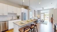 This well-designed single-floor residence offers a bright and contemporary living experience with a cohesive neutral color palette and warm hardwood-style flooring throughout the main living areas. The open-concept kitchen is a standout feature, showcasing white shaker cabinetry, a classic subway tile backsplash, stainless steel appliances including a gas range and French door refrigerator, and a central island with a quartz countertop and pendant lighting overhead — ideal for both meal preparation and casual dining. The kitchen flows seamlessly into the living area, which benefits from large windows and a ceiling fan, creating an airy, connected atmosphere. The bedrooms are generously sized and carpeted for comfort, each featuring oversized windows that fill the rooms with natural light and provide views of the surrounding greenery. The bathrooms are finished with clean, modern details, including white vanity cabinetry with quartz countertops, large-format tile surround in the tub/shower combination, and rich hardwood flooring. A stacked in-unit washer and dryer adds everyday convenience. With high ceilings, recessed lighting, and direct outdoor access from the living area, this residence combines functional design with a warm, inviting ambiance.