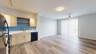 Located at 120 W Mishawaka Ave in Mishawaka, Indiana, this single-story unit offers a clean, contemporary design highlighted by wood-look luxury vinyl plank flooring that flows consistently throughout the space. The open-concept layout connects the kitchen directly to the living area, creating an inclusive and functional floor plan.

The kitchen is well-appointed with light maple cabinetry, white countertops, and a bold blue accent wall that adds a modern contrast. Black appliances — including a refrigerator, range, microwave, and dishwasher — complement the cabinetry, while track lighting overhead provides ample illumination. Open shelving adds additional storage and display space.

The living area is generously proportioned, featuring a ceiling fan and a large sliding glass door fitted with vertical blinds that allows natural light to fill the space and provides outdoor access. The neutral gray tones on the walls create a calm, versatile backdrop throughout.

The bedroom is bright and well-sized, with a window offering natural light and direct access to a spacious walk-in closet outfitted with wire shelving and hanging rods along two walls, providing substantial storage capacity. Additional rooms maintain the same neutral palette and flooring, contributing to the unit's cohesive and functional overall character.