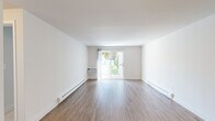 Located at 1982 Village Green S in East Providence, Rhode Island, this single-floor, two-bedroom, one-bathroom unit offers a clean and functional layout across a comfortably sized floor plan. The living area serves as the heart of the space, featuring smooth hardwood-style flooring, crisp white walls, and a sliding glass door that frames outdoor greenery and fills the room with natural light. Baseboard heating runs throughout, and a wall-mounted air conditioning unit provides year-round climate control.

The galley-style kitchen is efficiently arranged with white cabinetry lining both sides, laminate countertops, a stainless steel sink, and an electric range, all illuminated by a window with blinds. Hardwood-style flooring continues through this space, maintaining a cohesive aesthetic.

Both bedrooms are carpeted and feature wall-mounted air conditioning units and baseboard heaters. Natural light enters through windows fitted with blinds. The primary bedroom includes a sliding double-door closet with a hanging rod, while the second bedroom offers its own dedicated closet. A hallway connects the rooms efficiently.

The bathroom features a full-size soaking tub with a shower rod, hardwood-style flooring, a window for ventilation, and baseboard heating, completing this straightforward and well-maintained unit.