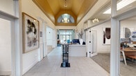 Located at 8732 Town and Country Blvd in Ellicott City, MD, this thoughtfully designed single-story commercial space offers a refined blend of professional functionality and welcoming comfort across a generously sized floor plan.

The entry foyer immediately impresses with its soaring vaulted ceiling accented by a bold gold finish, an arched transom window, elegant chandelier lighting, and large-format tile flooring. A sleek reception desk anchors the space, setting a polished first impression.

Adjacent to the entry, private offices feature warm wood desks, carpeted floors, and glass-paneled doors that allow natural light to flow between rooms. A dedicated workspace corridor connects multiple individual offices, each equipped for professional use with built-in cabinetry and workstation setups.

The lounge area is a standout, showcasing a dramatic floor-to-ceiling stacked stone fireplace beneath vaulted ceilings, rich hardwood floors, wainscoting, and expansive French doors that open directly onto an outdoor deck — flooding the room with natural light and outdoor views.

A full kitchen supports the space with gray shaker cabinetry, granite countertops, stainless steel appliances, and hardwood-style flooring. A cozy banquette nook with a slatted room divider provides an intimate seating area ideal for informal meetings or breaks.

Throughout, the space maintains a cohesive aesthetic of clean white walls, classic millwork, and curated artwork.