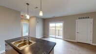 Located on Sherwood Ave in Holland, Michigan, this single-floor residence offers a thoughtfully designed layout that balances functionality and comfort. The open-concept living and kitchen area forms the heart of the space, where light wood-look flooring flows seamlessly underfoot and warm neutral tones on the walls create a welcoming ambiance. Pendant lighting above the kitchen island adds a contemporary touch, while the dark countertops and light-toned cabinetry provide a striking visual contrast. The kitchen features ample upper and lower cabinet storage, a double-basin sink, and dedicated counter workspace throughout. A sliding glass door in the living area opens to a private balcony with railing, allowing natural light to fill the space and offering views of the surrounding landscape. The bedrooms are carpeted for added comfort, with large windows that bring in additional natural light and outdoor scenery. The unit includes two bathrooms: one featuring a full soaking tub and shower combination, and a second with a standalone walk-in shower — both finished with clean white fixtures and vanities. Consistent use of neutral warm-beige wall tones and white trim throughout the unit ties the overall aesthetic together, creating a cohesive and move-in ready living environment.