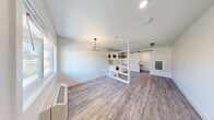 Located at 615 Jawdin Ave in Richland, Washington, this efficiently designed single-floor unit makes excellent use of its compact footprint. The open main living area is finished with light gray wood-look luxury vinyl plank flooring and crisp white walls, creating a clean, modern aesthetic. A decorative chandelier adds a touch of elegance, while a wall-mounted HVAC unit ensures year-round comfort. Natural light filters in through a large window near the entry door.

A distinctive open-cube shelving unit serves as a stylish room divider, visually separating the living area from the kitchen zone without sacrificing openness. The kitchen features white shaker-style cabinetry with matte black hardware, a sleek black undermount sink, a black glass cooktop, a range hood, and a full-size refrigerator. The eye-catching geometric tile backsplash in a white-and-black elongated hexagon pattern extends to the ceiling, adding bold visual interest. A dark floating shelf above provides additional storage.

The bathroom is a standout, fully clad in white penny-round wall tiles and contrasting dark penny-round floor tiles. It is designed with accessibility in mind, featuring grab bars, a wall-mounted sink, a toilet, and an open wet-room shower area. A sliding barn door provides a stylish entry to this well-appointed space.
