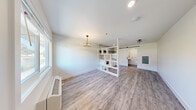 Located at 615 Jawdin Ave in Richland, Washington, this efficiently designed single-floor unit makes excellent use of its compact footprint. The open main living area is finished with light gray wood-look luxury vinyl plank flooring and crisp white walls, creating a clean, modern aesthetic. A decorative chandelier adds a touch of elegance, while a wall-mounted HVAC unit ensures year-round comfort. Natural light filters in through a large window near the entry door.

A distinctive open-cube shelving unit serves as a stylish room divider, visually separating the living area from the kitchen zone without sacrificing openness. The kitchen features white shaker-style cabinetry with matte black hardware, a sleek black undermount sink, a black glass cooktop, a range hood, and a full-size refrigerator. The eye-catching geometric tile backsplash in a white-and-black elongated hexagon pattern extends to the ceiling, adding bold visual interest. A dark floating shelf above provides additional storage.

The bathroom is a standout, fully clad in white penny-round wall tiles and contrasting dark penny-round floor tiles. It is designed with accessibility in mind, featuring grab bars, a wall-mounted sink, a toilet, and an open wet-room shower area. A sliding barn door provides a stylish entry to this well-appointed space.