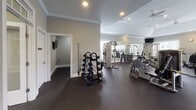 Located at Abberly Green in Mooresville, NC, this fitness center is a thoughtfully designed, single-floor facility built to support a full range of workout routines. The space features a tray ceiling with a ceiling fan and recessed lighting, contributing to an open, airy atmosphere. Warm gray walls, crown molding, and white-trimmed windows lend a polished, welcoming aesthetic uncommon in typical gym environments.

The cardio zone is lined with multiple treadmills and elliptical machines positioned along a bank of large windows, offering natural light and outdoor views that make workouts more enjoyable. A wall-mounted television adds further entertainment. The strength training area is generously equipped with cable machines, a power rack, and a selection of benches and selectorized weight stations suited for a variety of exercises. A well-stocked dumbbell rack provides options for free weight training.

A dedicated entry vestibule features a body weight scale and a rack of medicine balls, making it a practical space for warm-ups and functional fitness. Large interior windows and glass doors connect this area visually to the main floor, creating a cohesive, open feel. Rubber flooring throughout ensures safety and durability. Full-length mirrors expand the visual space and support proper form during exercise, completing this comprehensive and well-appointed fitness facility.